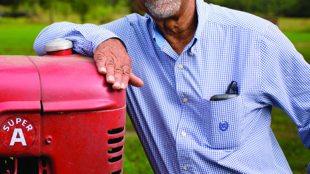 Smiling man in gingham dress shirt leans on a tractor