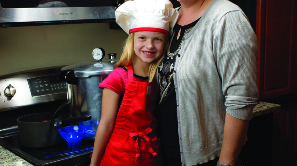 A little girl in a white chef’s hat stands beside her mother