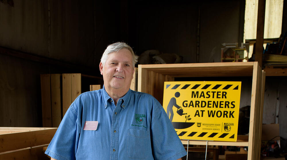 Paul Cavanaugh standing in front of a sign that reads Master Gardeners at Work.