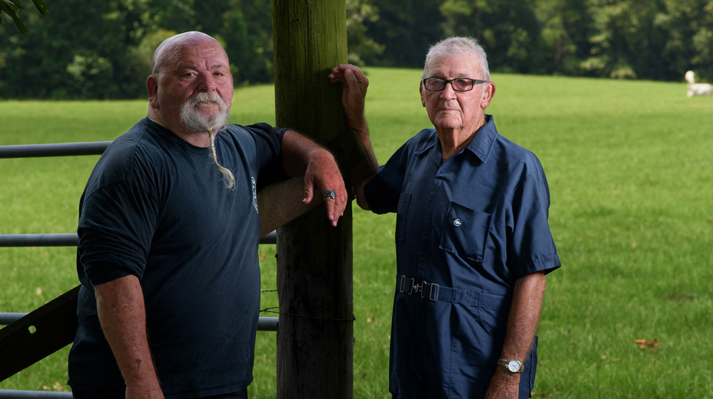 An elderly man stands next to his son.