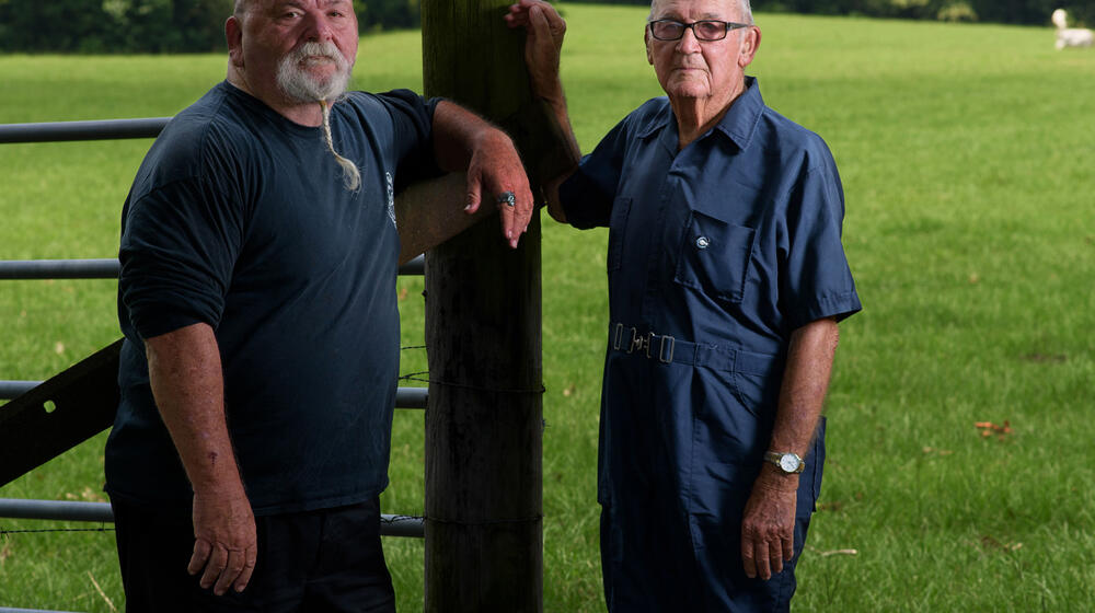 An elderly man stands next to his son.