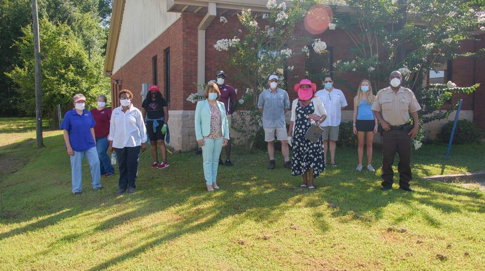 A group of 11 men and women wearing masks stand in front of a brick building.