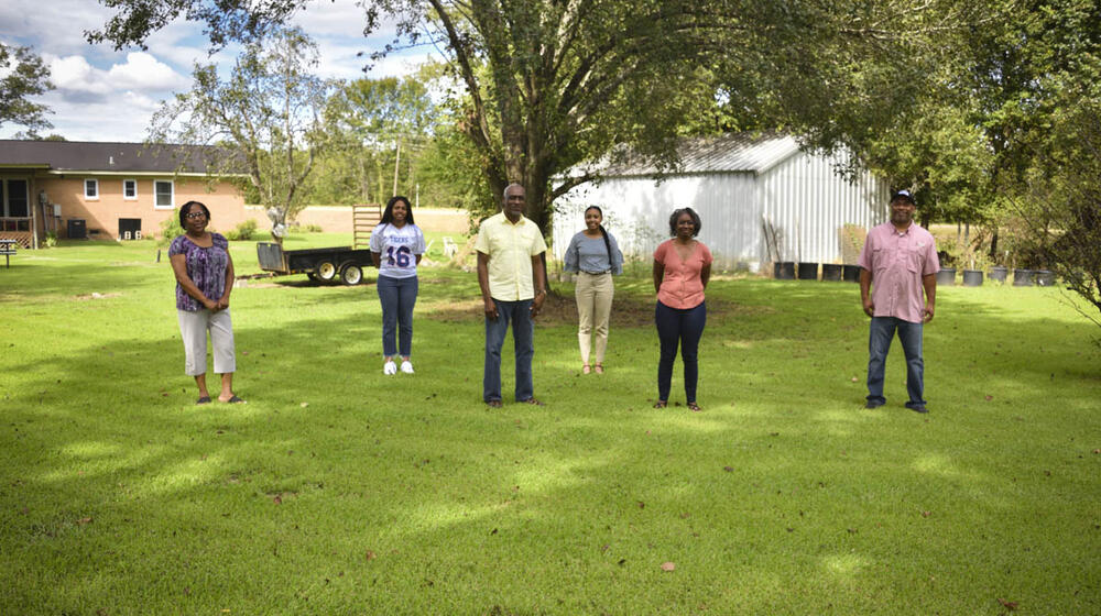 Four women and two men stand spaced out in green grass.