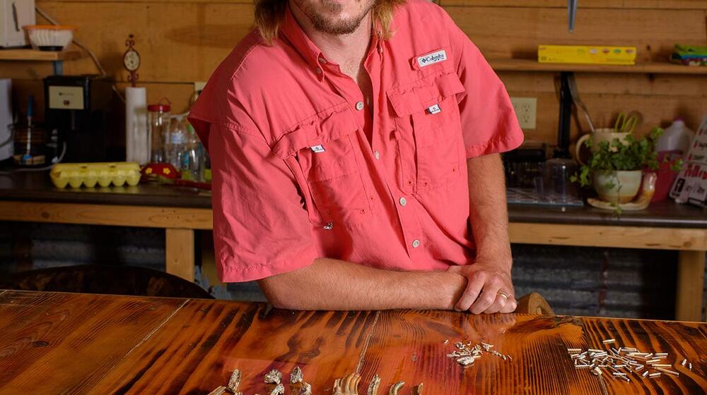 A man with glasses standing behind a table with shells, teeth, and bones on it.