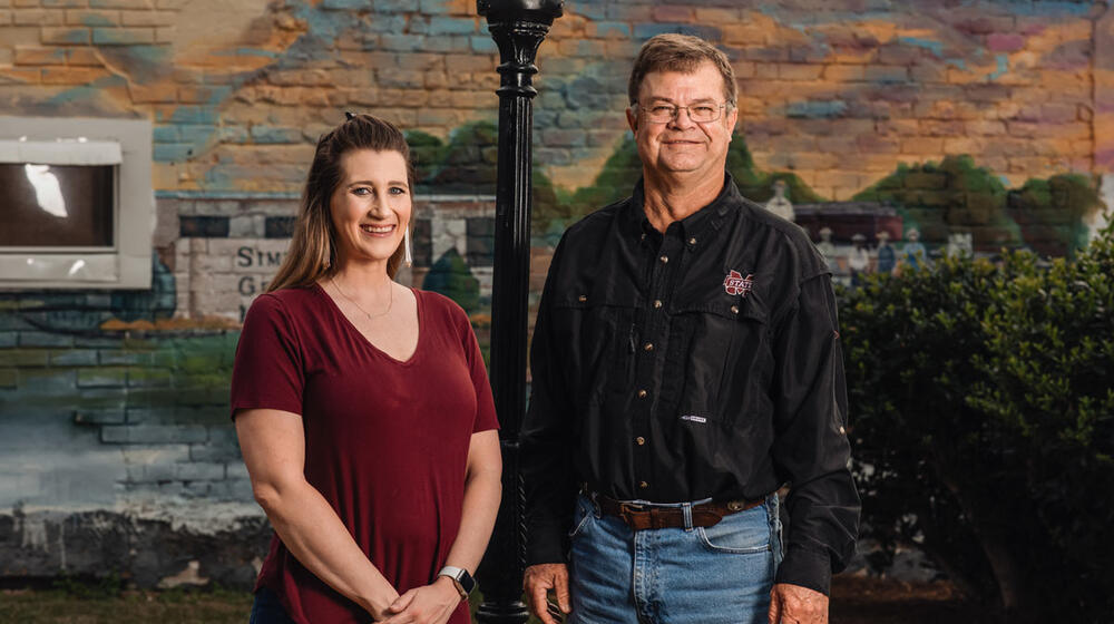 A woman and a man standing in front of a mural and lamppost.