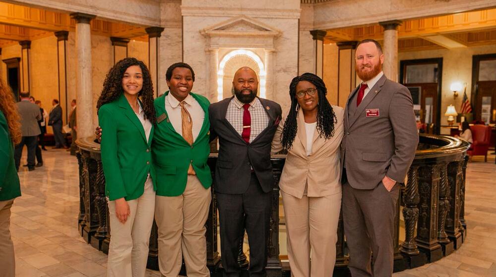 Five people, including two teens in green 4-H blazers, smile for a group photo.