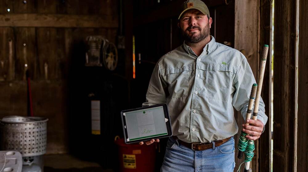 A man stands in a wooden shed holding parts to a soil sensor system.