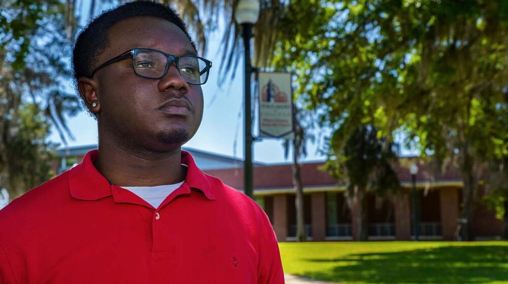 A young man, wearing glasses and a red shirt, standing outside and looking over the horizon.