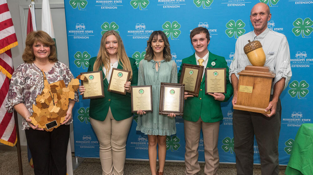 A group of five people, each holding awards, smiling.