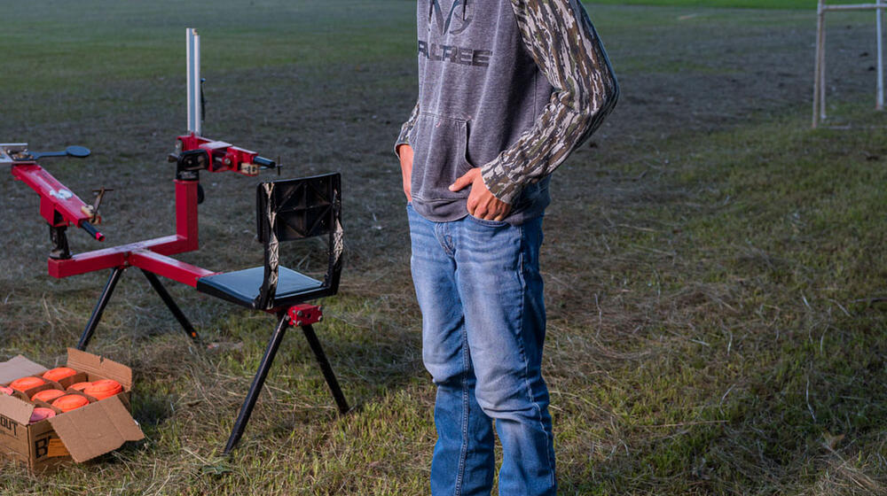 A boy standing beside a sport shooting range smiling.