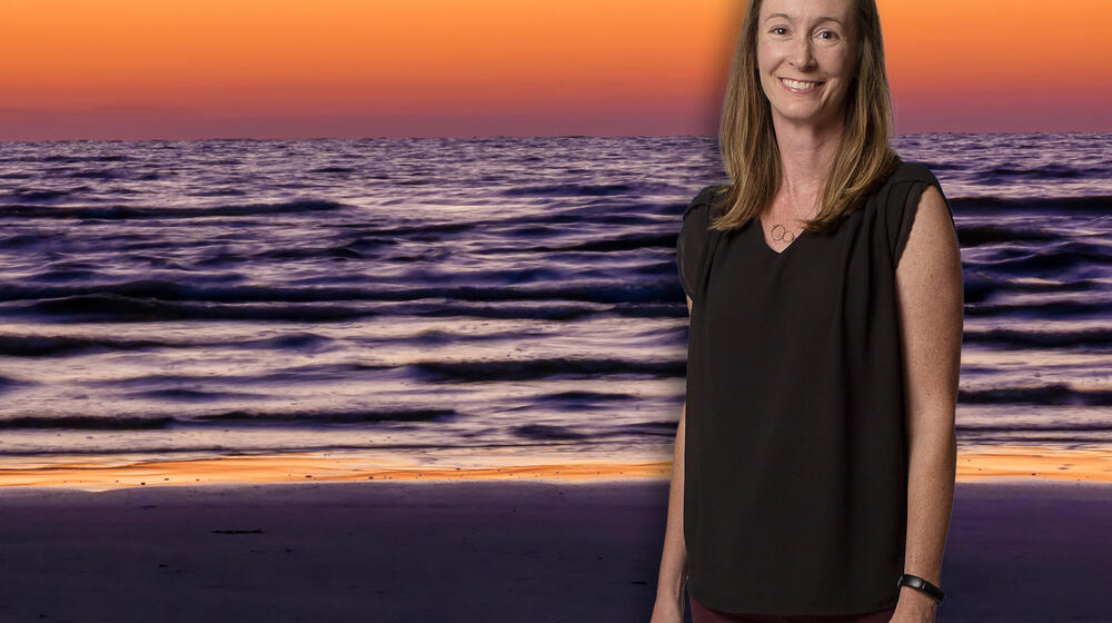 A woman, smiling, standing in front of the ocean