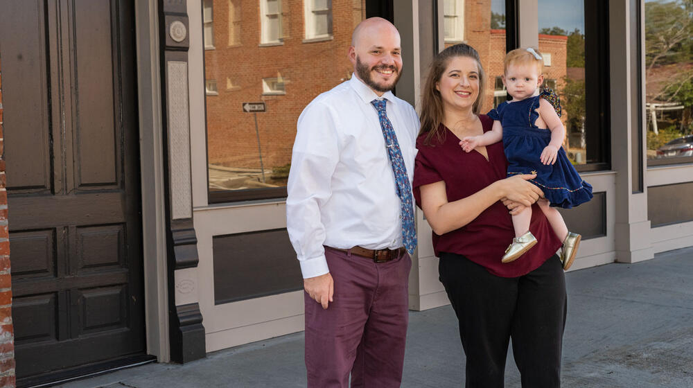 A man, woman, and child standing outside, smiling in front of a building.