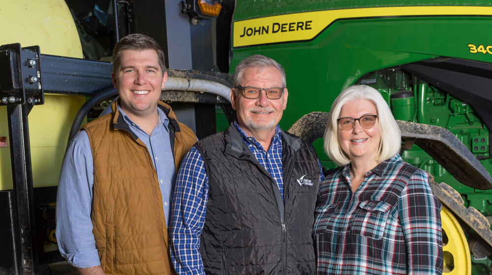 Two men and one woman standing in front of a green tractor
