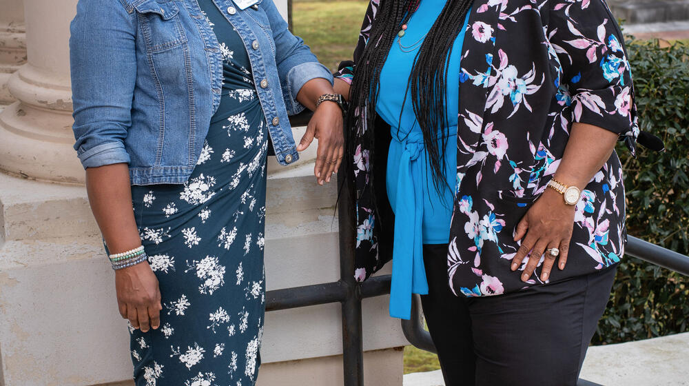 Two women standing in front of a column, smiling.
