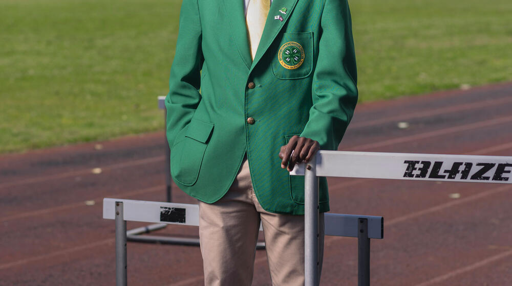 A young man wearing a green 4-H blazer stands smiling on a running track.