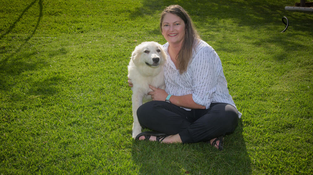A woman, smiling, sitting with her arms around a large dog.