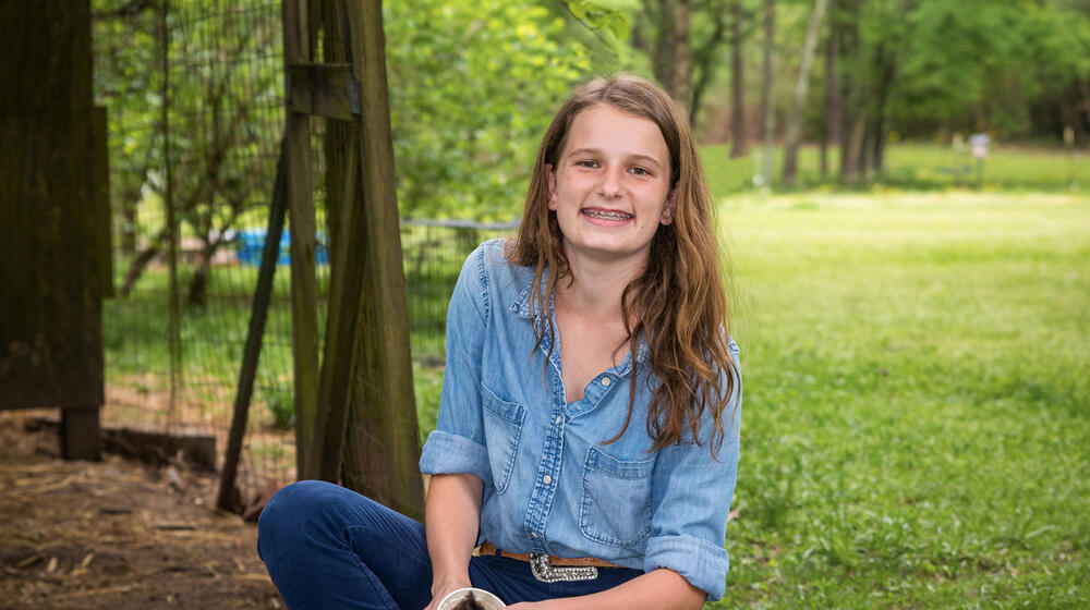 A girl wearing denim smiles as she feeds her chickens.