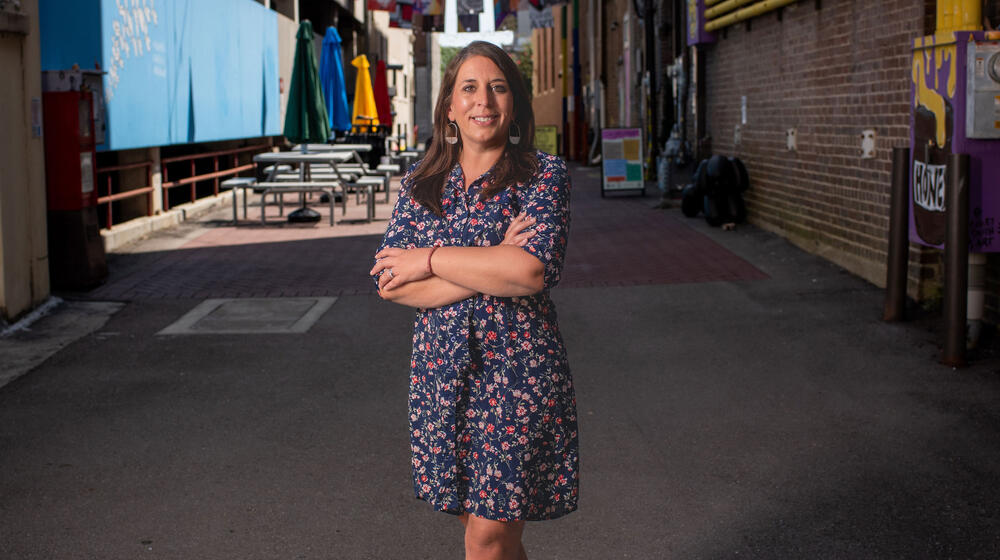 A woman smiling and standing on a street in front of many colorful, bright flags.
