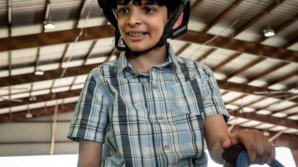 A smiling young man astride a horse and wearing a helmet.