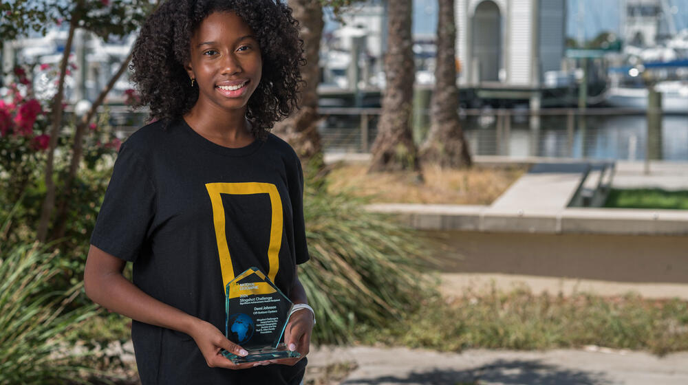 A young woman smiling and holding a trophy.