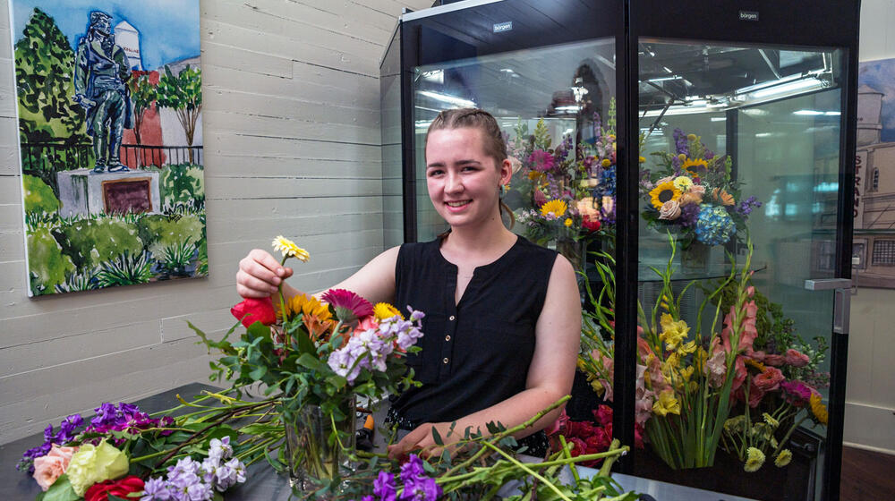 A young woman smiling while arranging a bouquet of flowers.