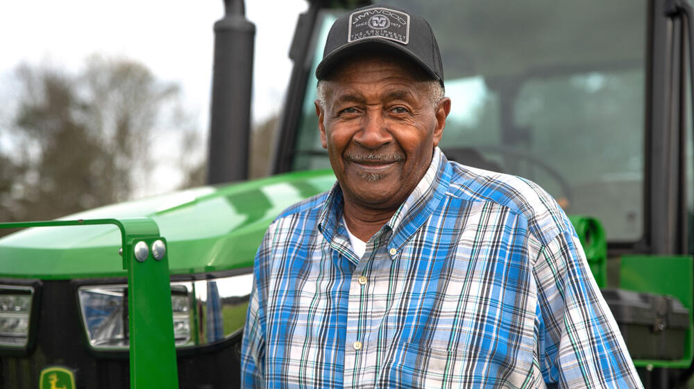 A smiling man standing in front of a green tractor.