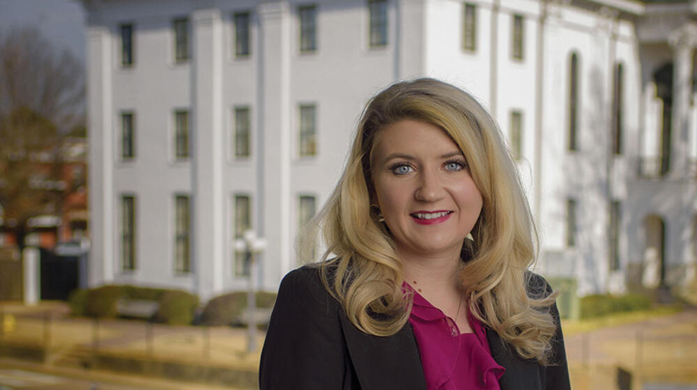 A woman rests her arm on the rail of a balcony.