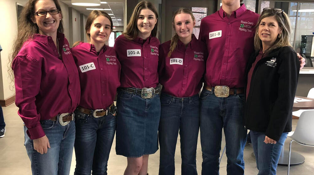 Six people, including two women, three girls, and one boy, wearing maroon polo shirts and smiling at the camera.