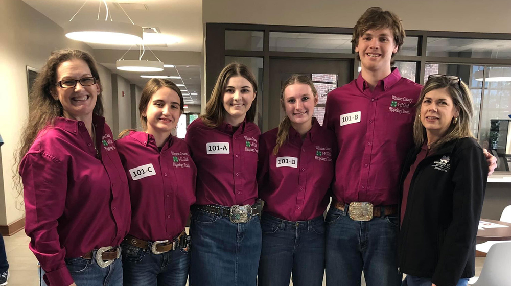 Six people, including two women, three girls, and one boy, wearing maroon polo shirts and smiling at the camera.
