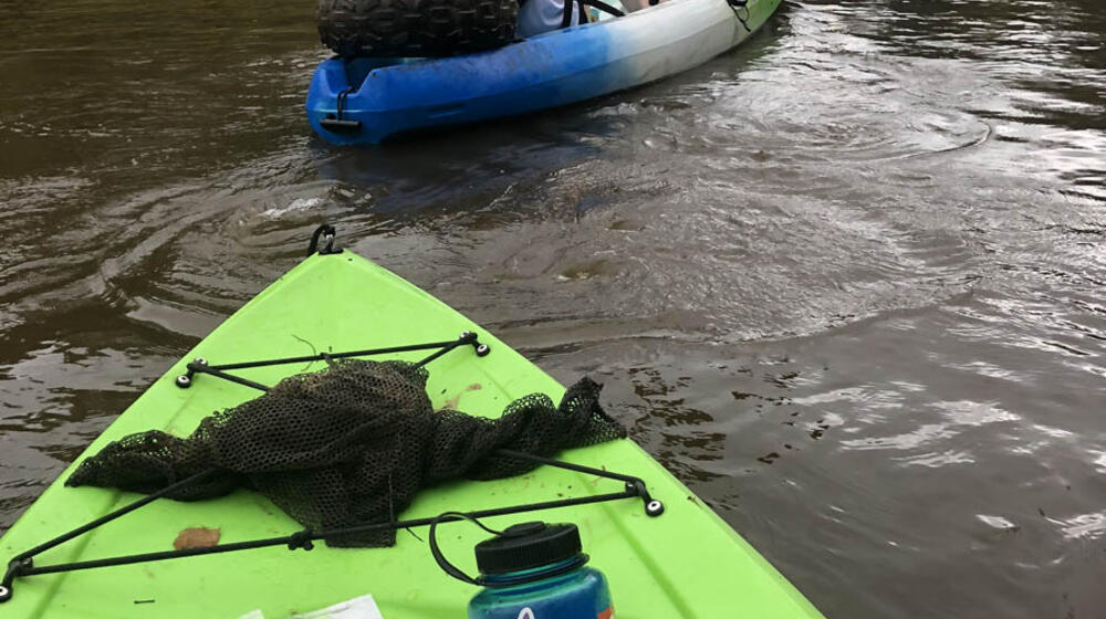 View from a green kayak of the back of two women paddling a kayak. 