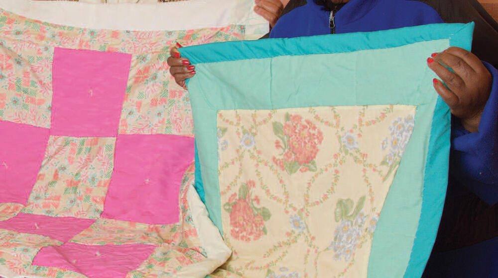 2 women hold up quilts.