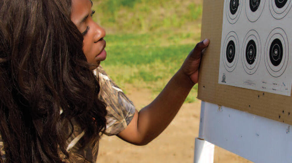 A young woman kneels down next to a board with targets.