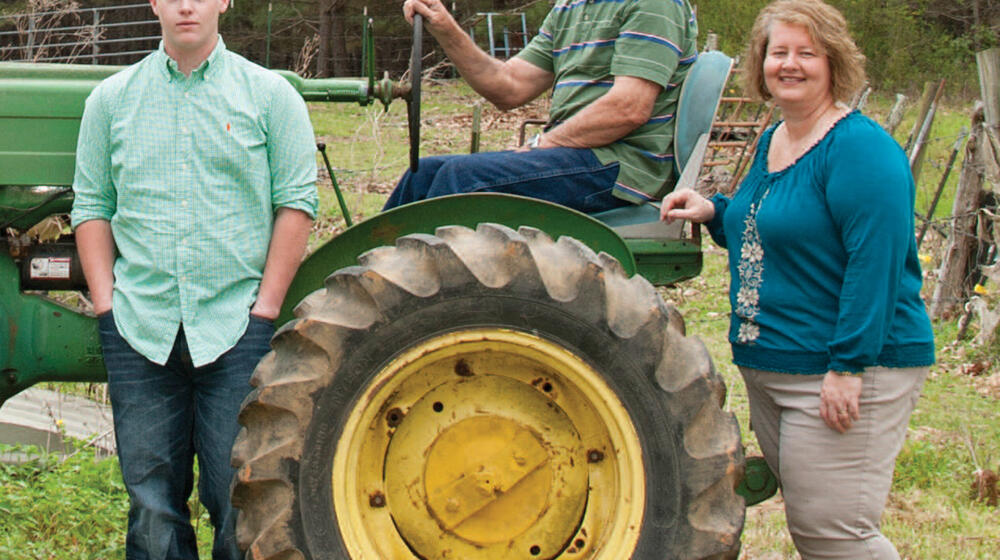 An older man, a woman, and a teenage boy around a green tractor.