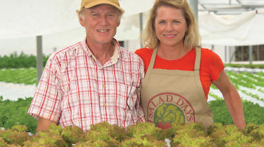A man and woman behind plants in a greenhouse.
