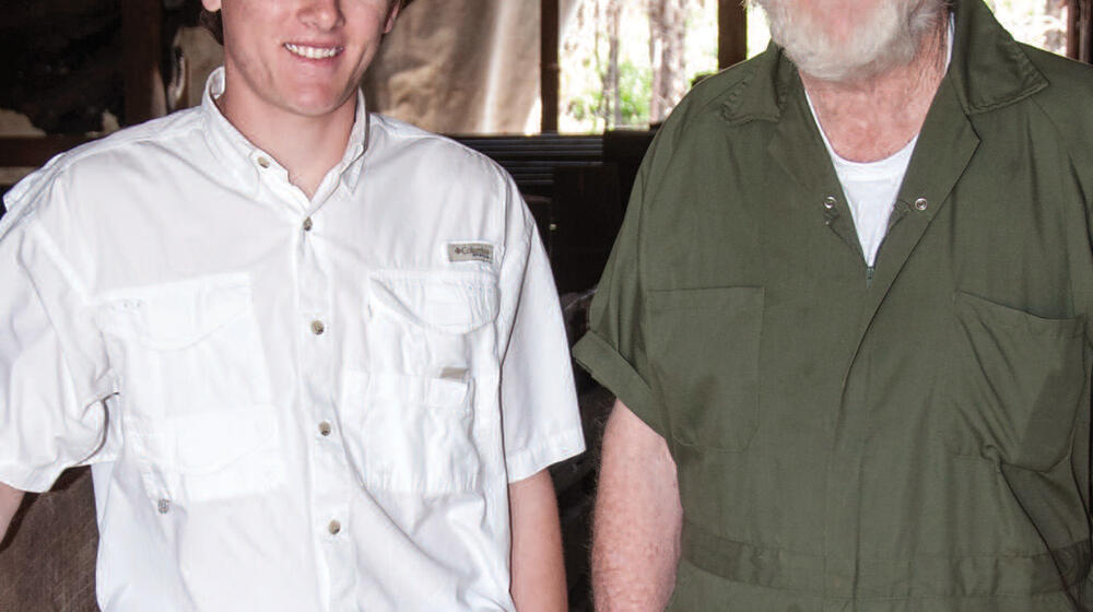 An older man and a young man stand next to each other smiling.