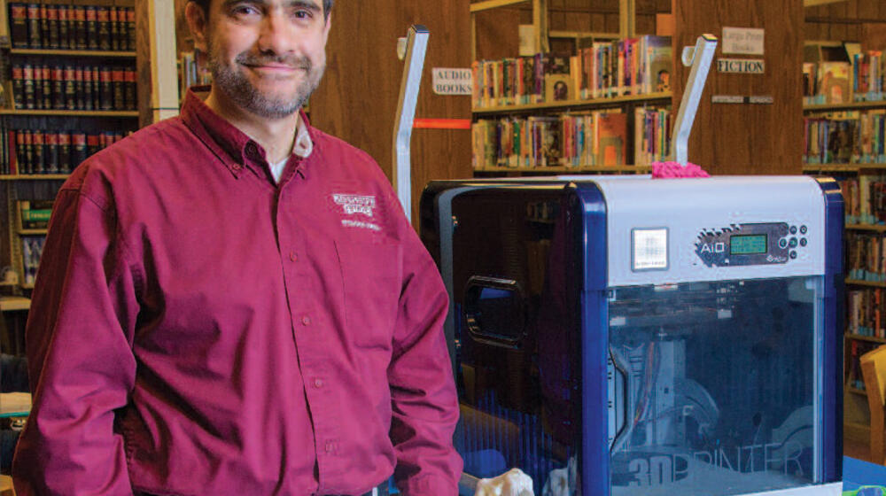 A man stands next to a 3D printer.