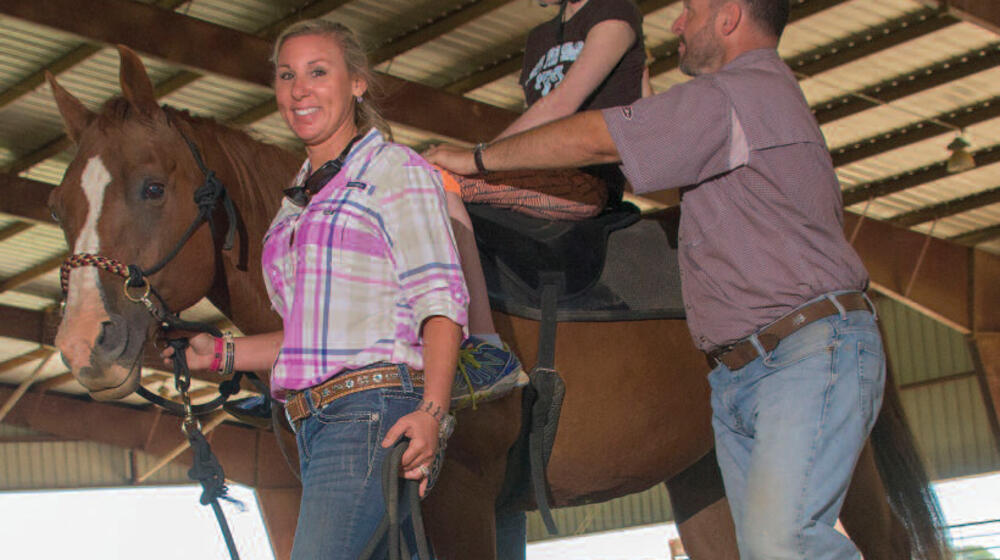 A girl on a brown horse led by a woman and man.