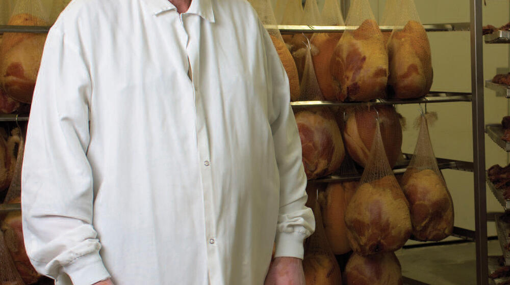 A man stands in front of a rack holding meat.