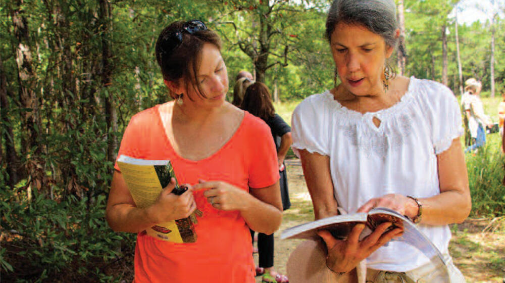 Two women walk and look at a book.