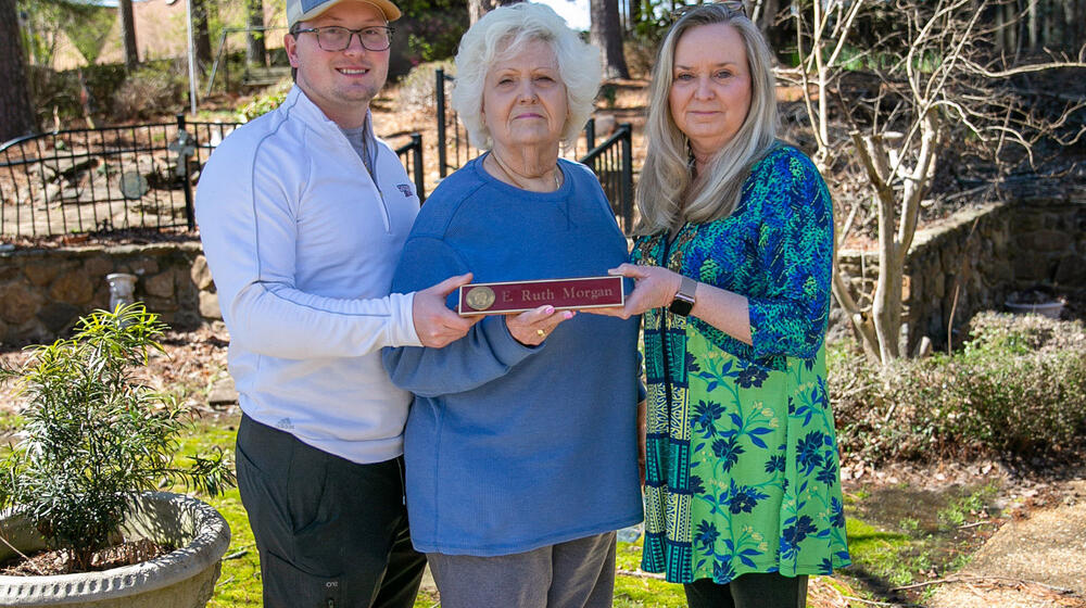 A woman, flanked by a young man and woman, holds a nameplate listing “E. Ruth Morgan.”