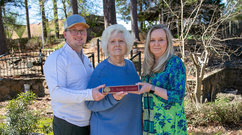 A woman, flanked by a young man and woman, holds a nameplate listing “E. Ruth Morgan.”