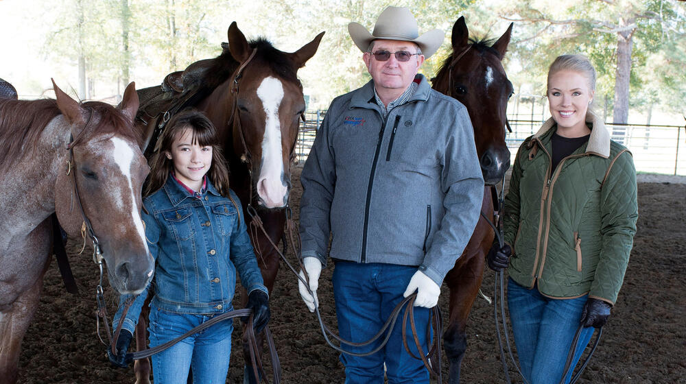 A man and two girls stand in a barn with three horses.