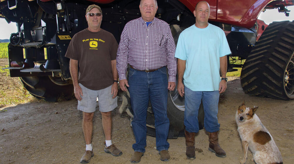 Three men and a dog stand in front of farm equipment.