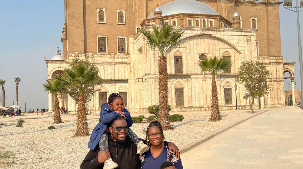 A Black man and woman standing with a boy and a girl in front of a mosque in the desert.